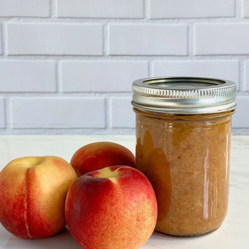 Roasted peach butter in a mason jar with fresh peaches next to it.