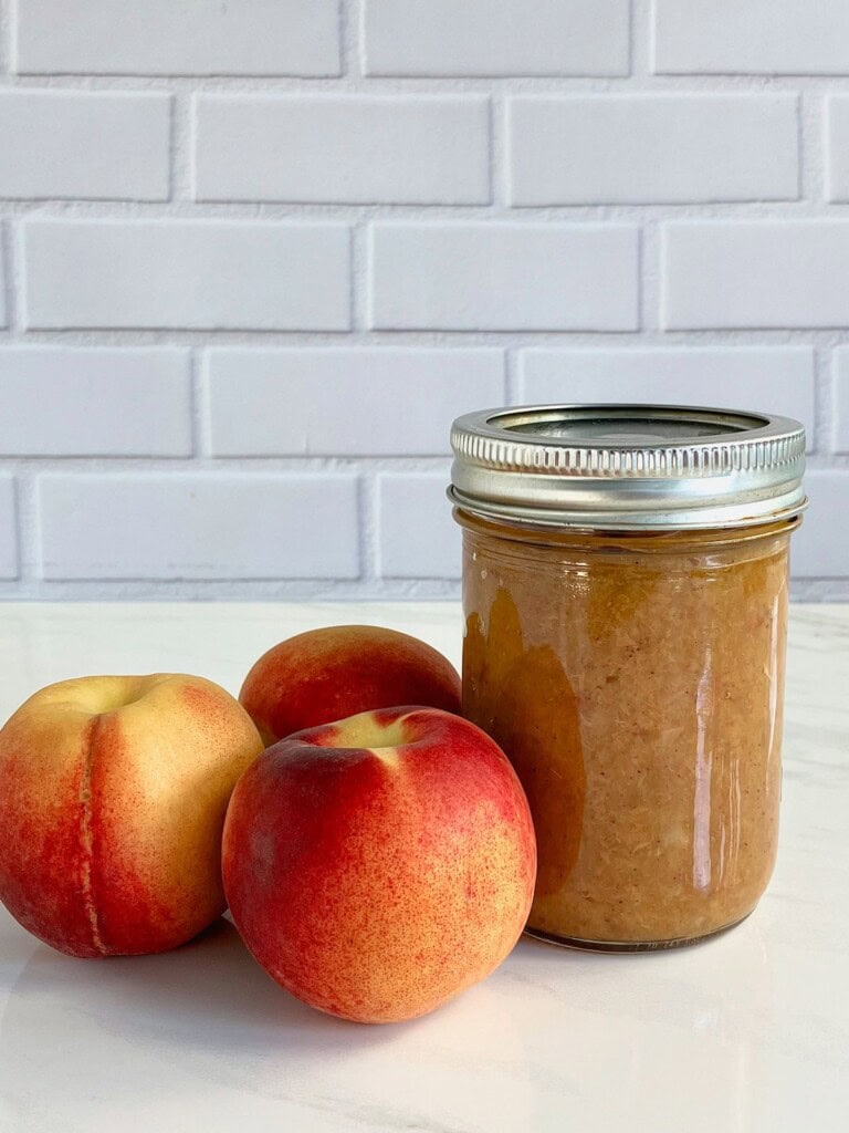 Roasted peach butter in a mason jar with fresh peaches next to it.