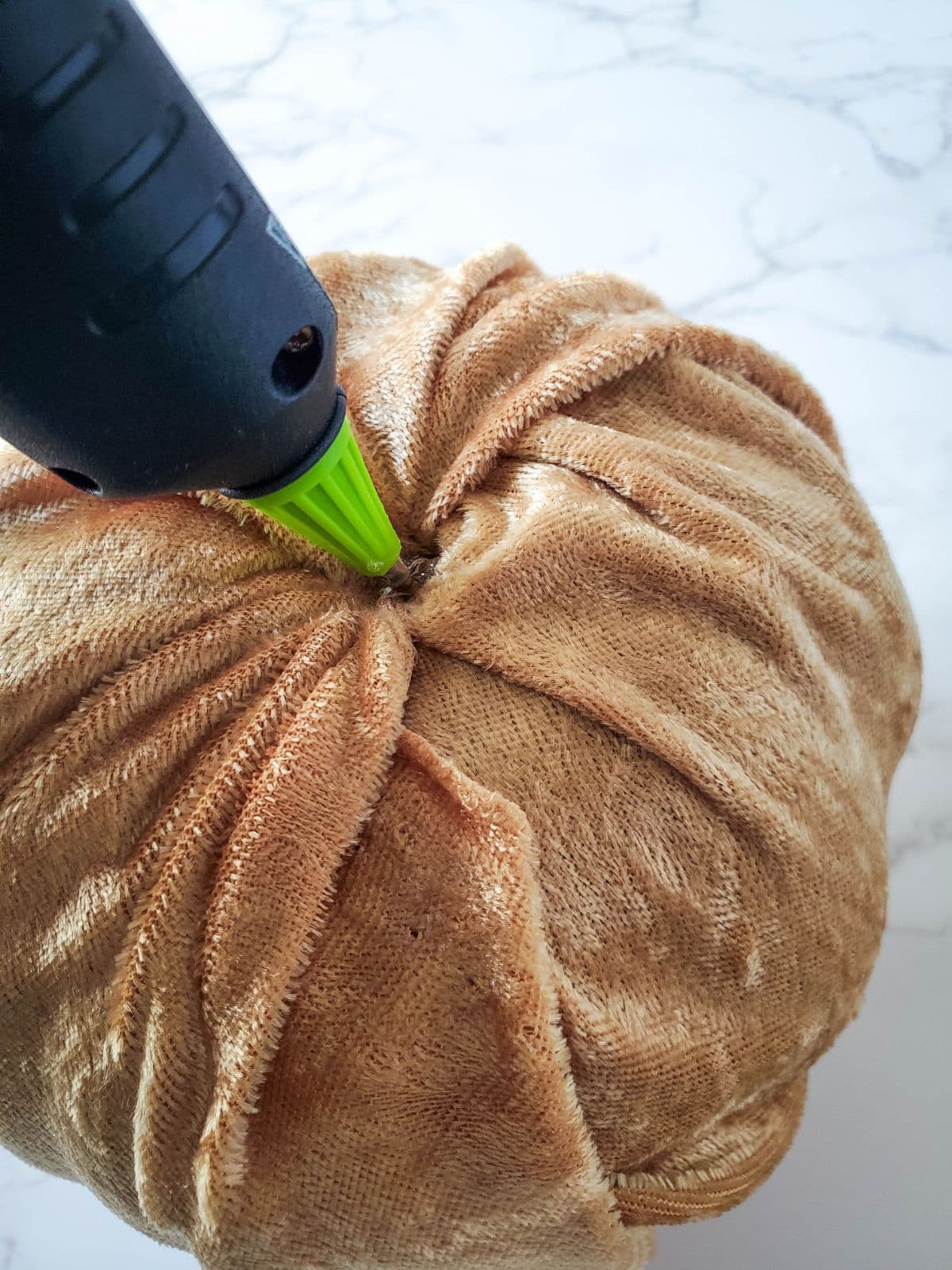 Adding hot glue to the hole in the pumpkin to hold the fabric and stem.