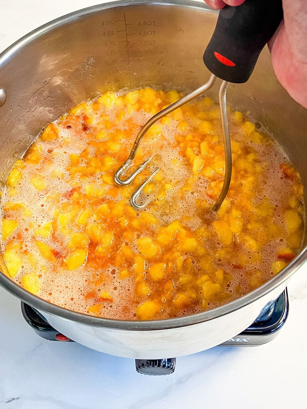 Mashing peaches with a potato masher.