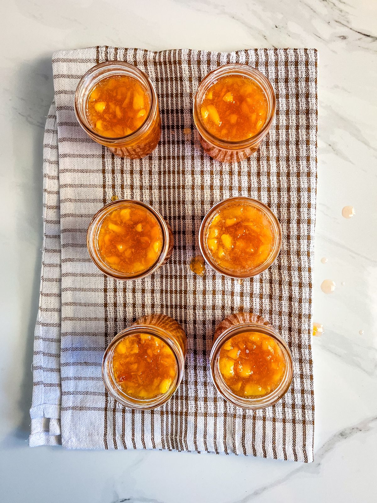 Half pint jars filled with homemade peach jam are sitting on a towel.