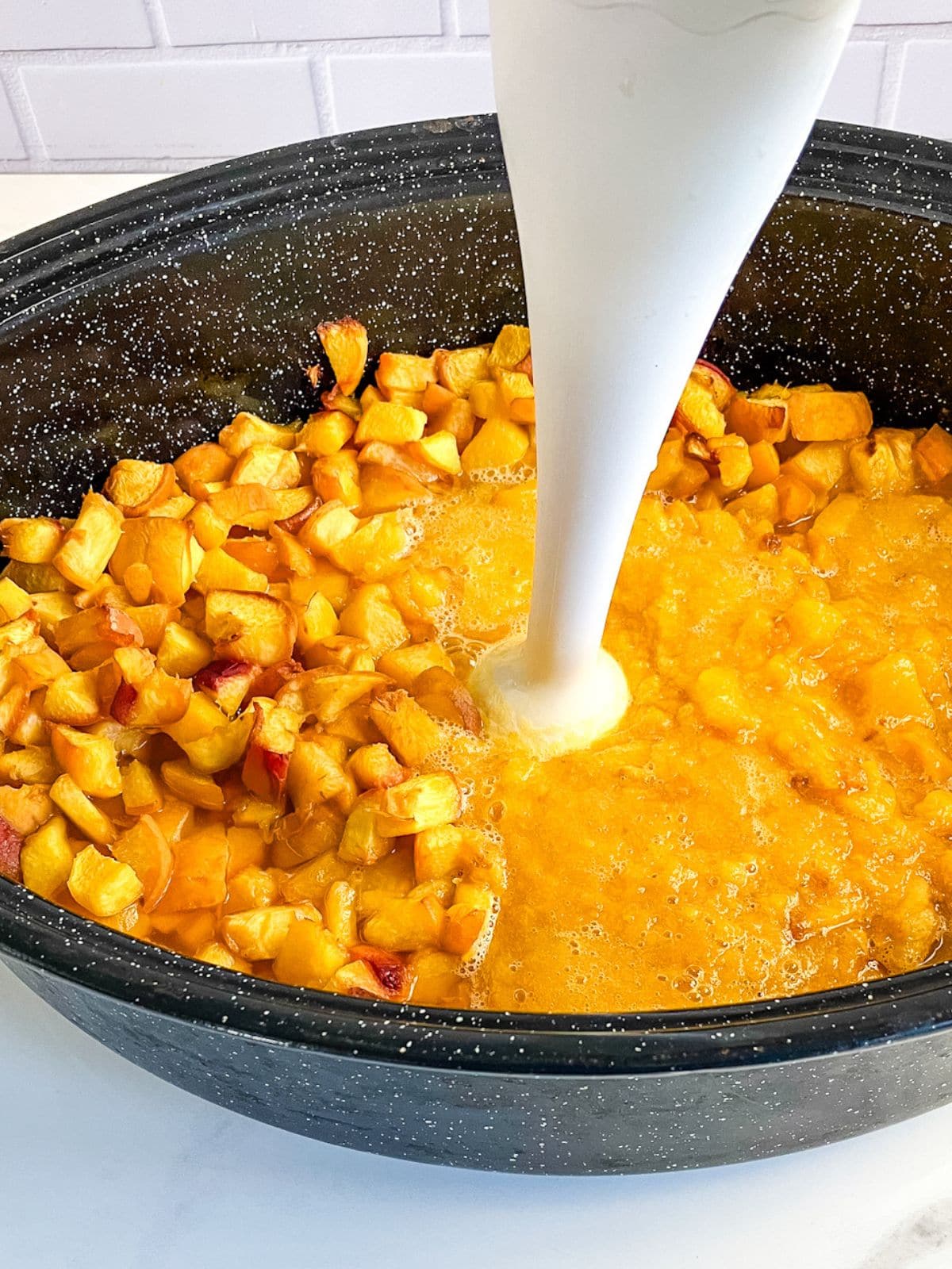 Pureeing cooked peaches in a roasting pan with a stick blender.