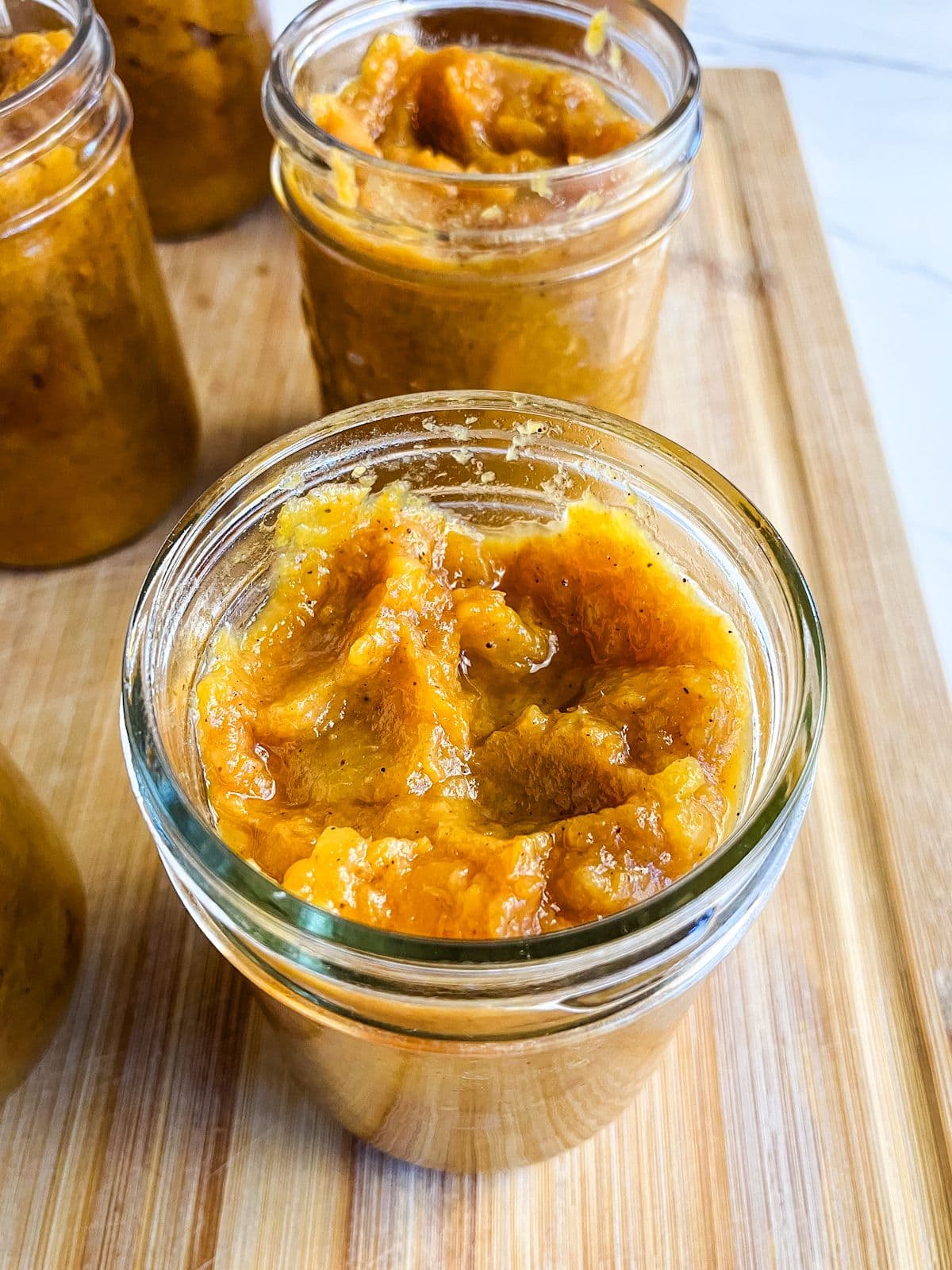 Homemade roasted peach butter ladled into mason jars.