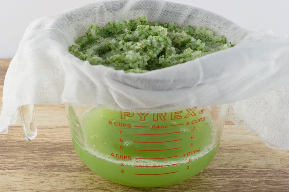 A fine mesh sieve lined with cheesecloth sitting in a large measuring cup. Pureed cucumbers poured into it and are draining into the cup.