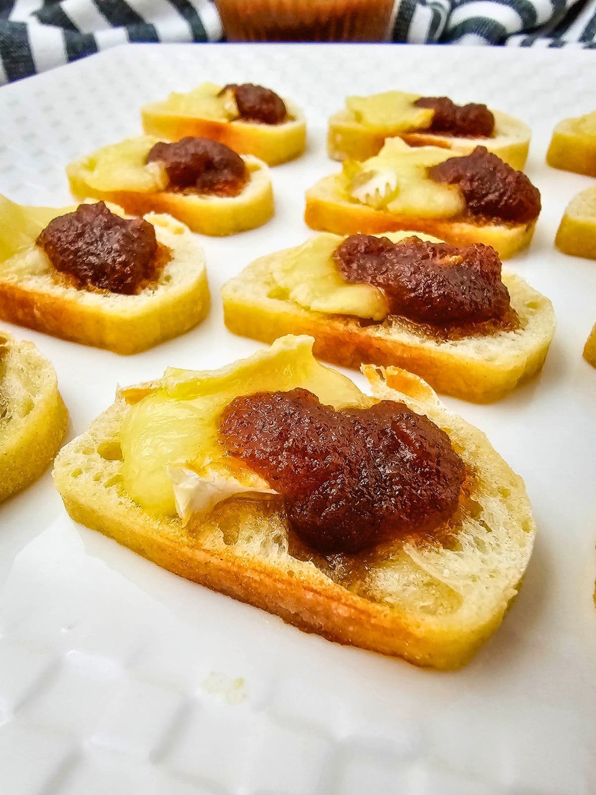 Homemade brie and apple butter crostini on a white platter.