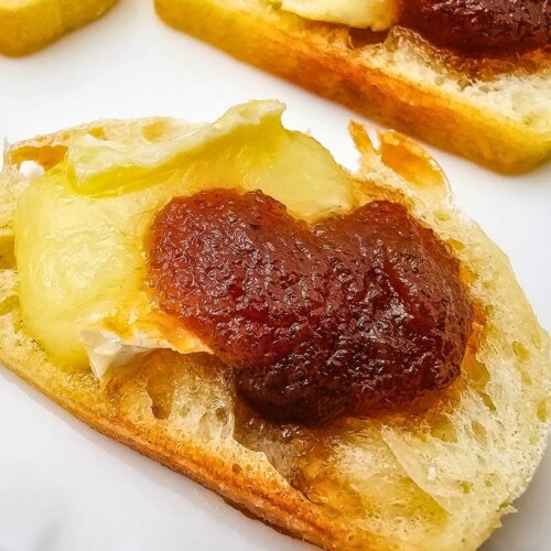 Apple butter and brie crostini on a white serving tray.