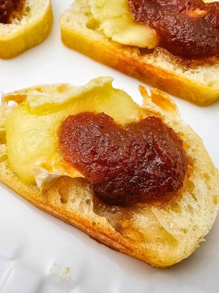 Apple butter and brie crostini on a white serving tray.