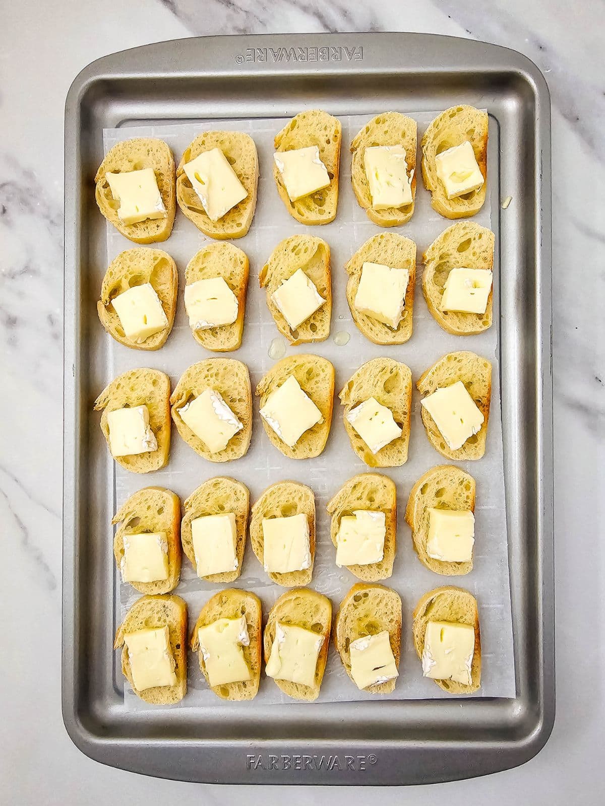 Slices of brie cheese on top of the toasted slices of baguette.