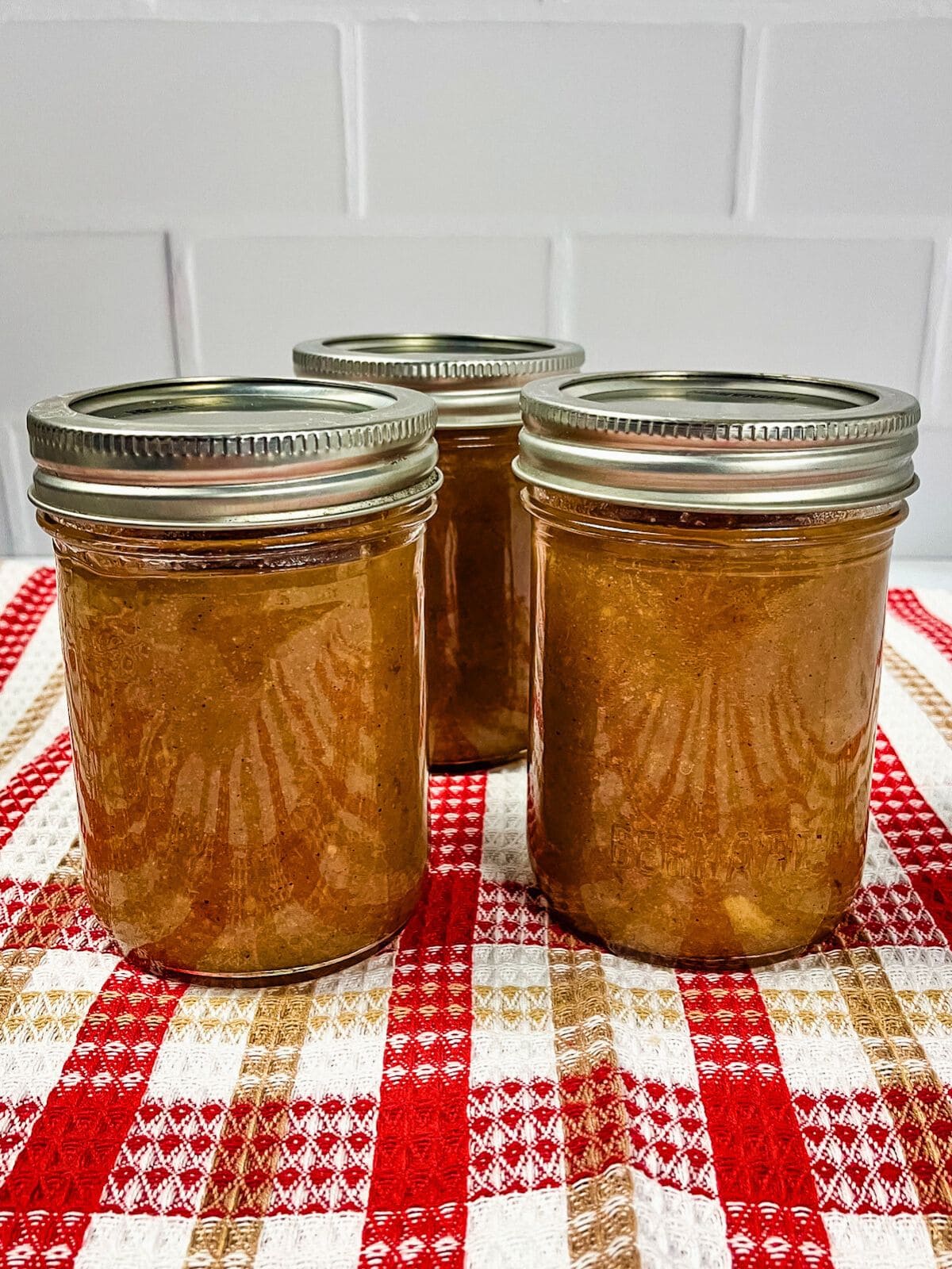 Three jars of homemade pear sauce cooling on the counter after canning.