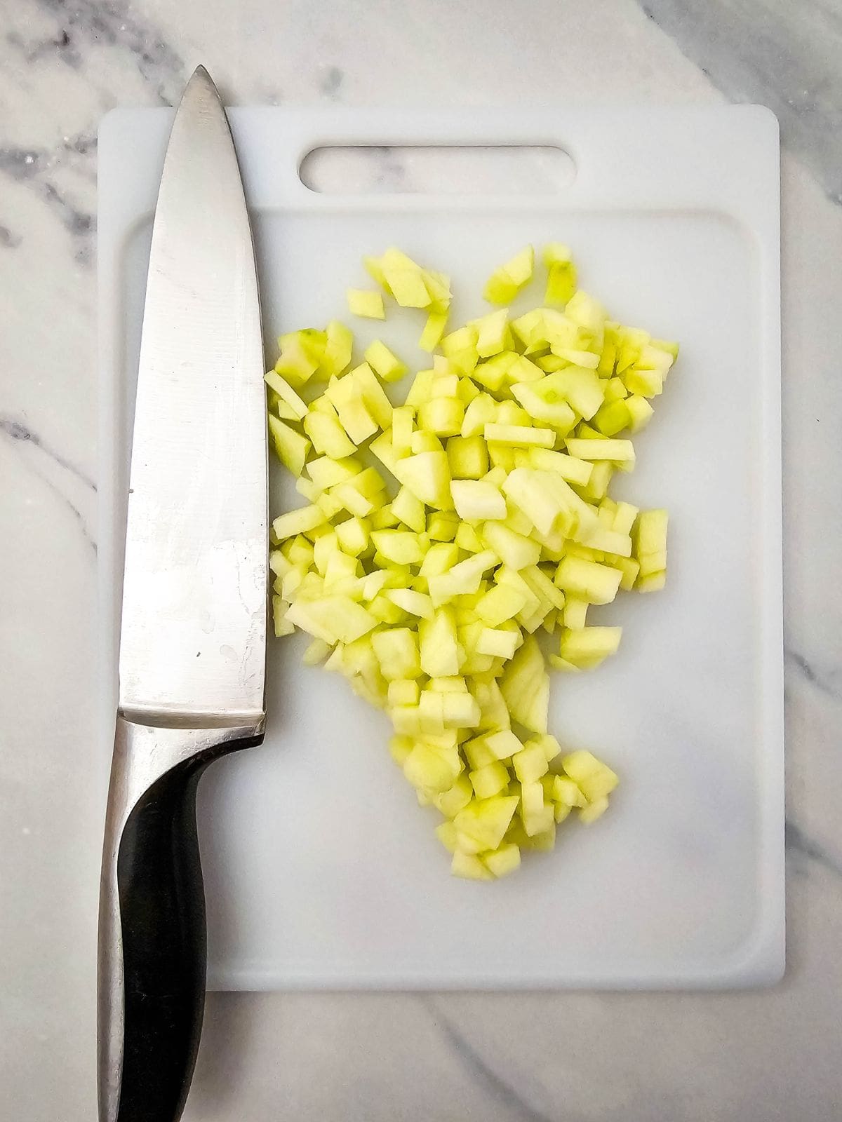 Diced apple on a cutting board next to a knife.