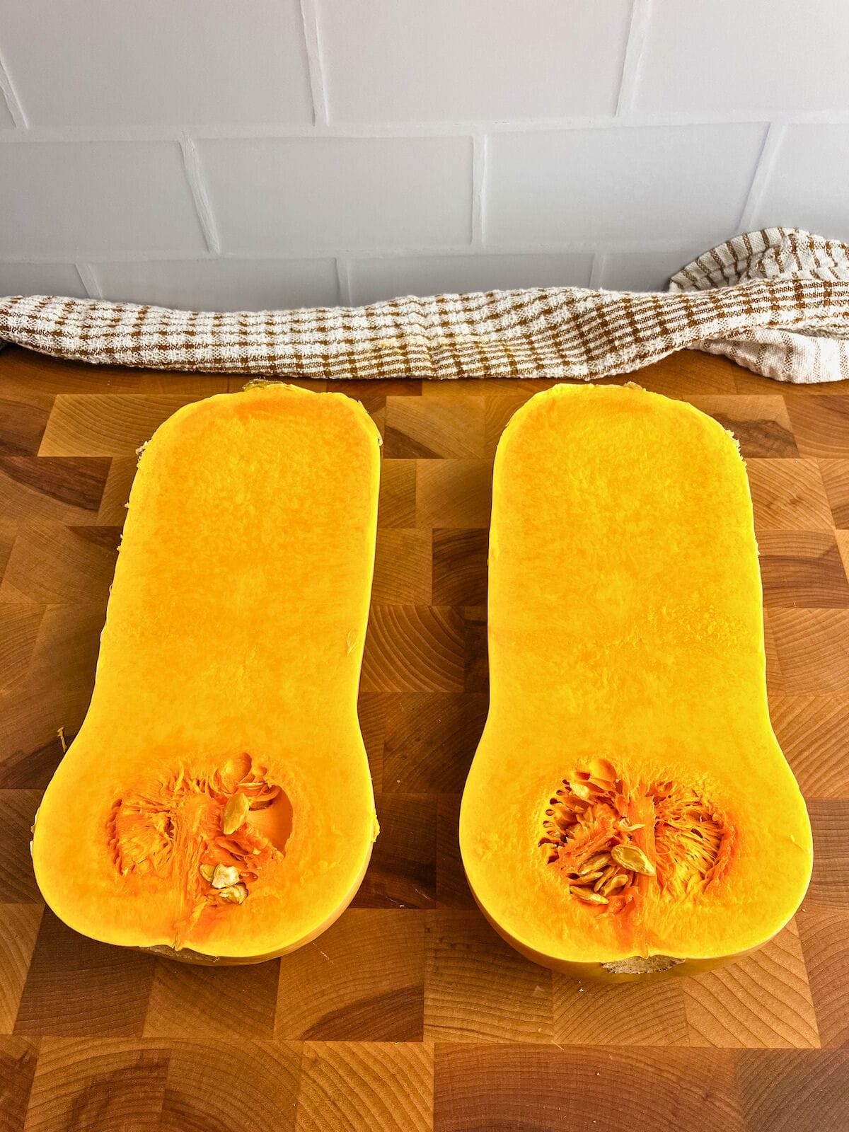 A butternut squash cut in half on a cutting board.