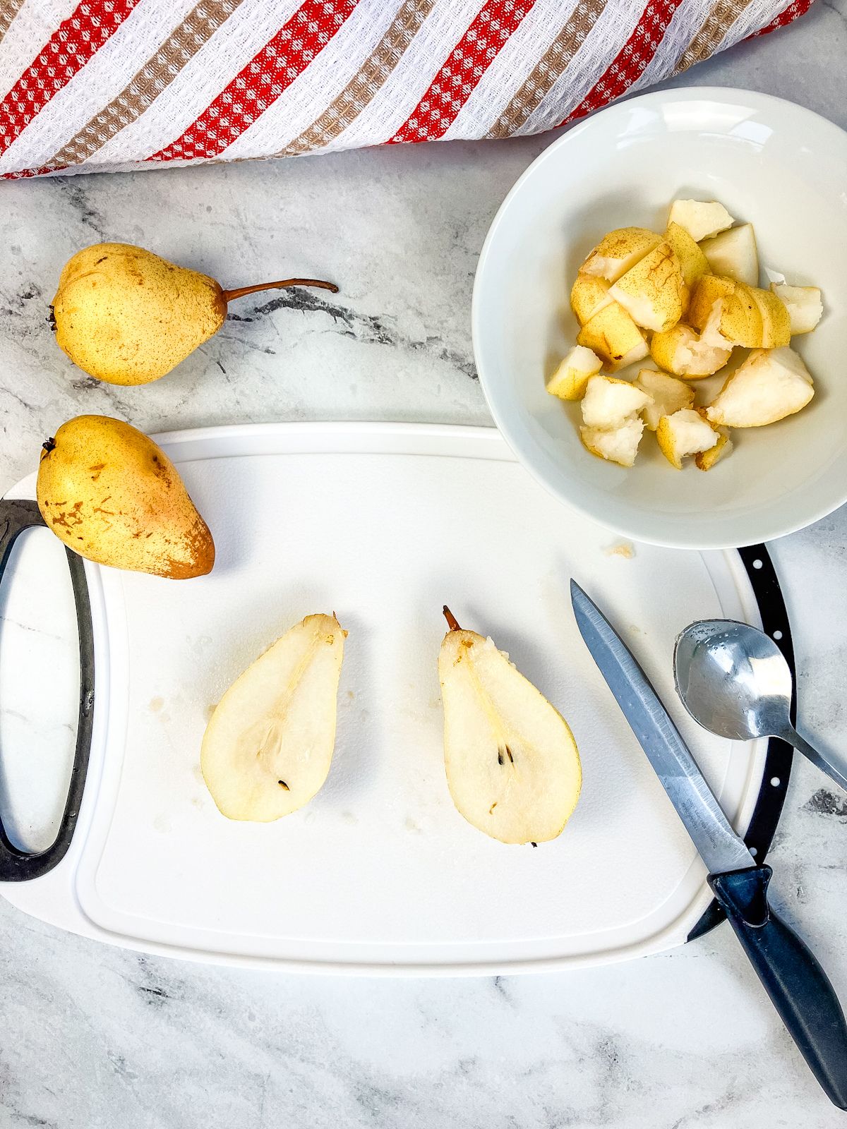 A white cutting board with cut pears and a bowl of diced pears.