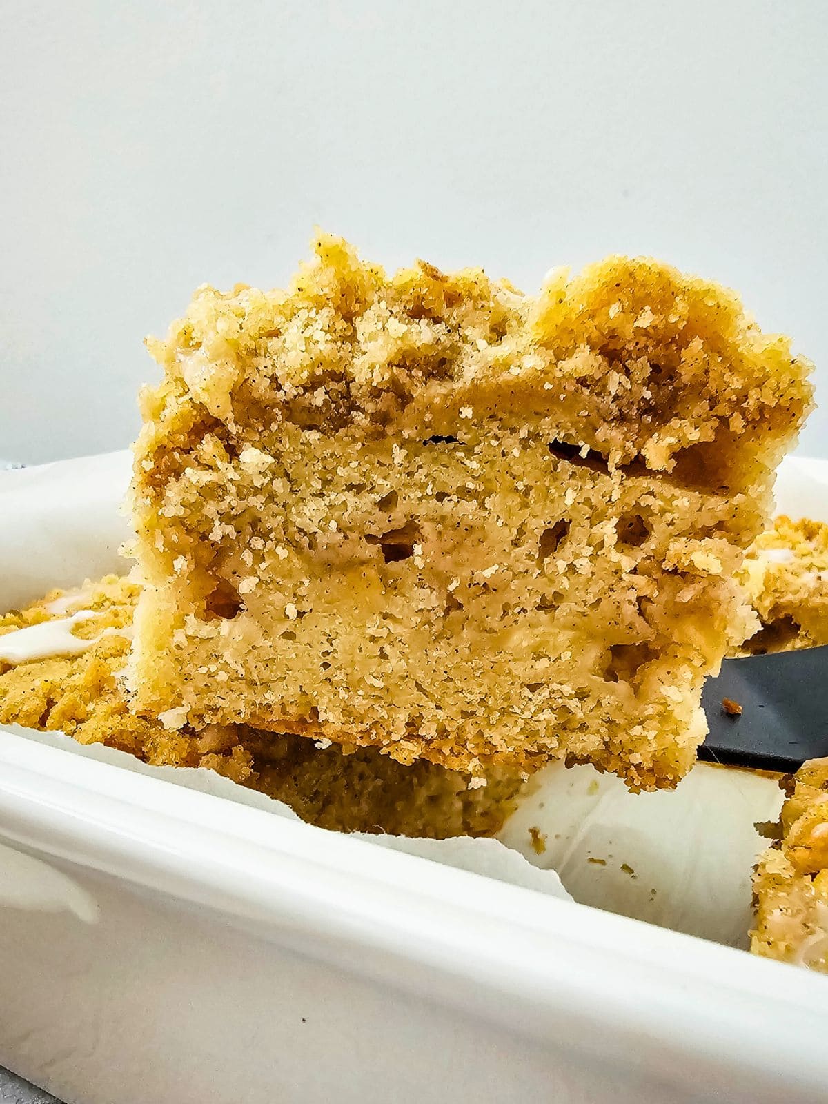 Lifting a slice of apple crumb cake out of the baking dish.
