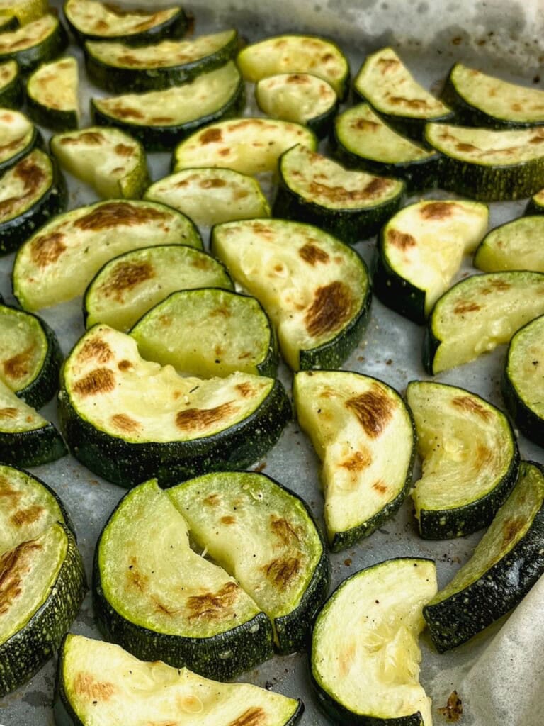 Sliced roasted zucchini on a sheet pan, baked and ready to eat.