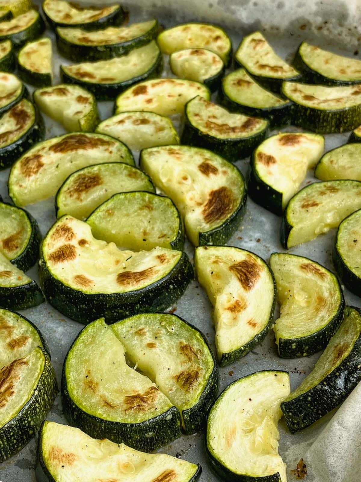 Sliced roasted zucchini on a sheet pan, baked and ready to eat.