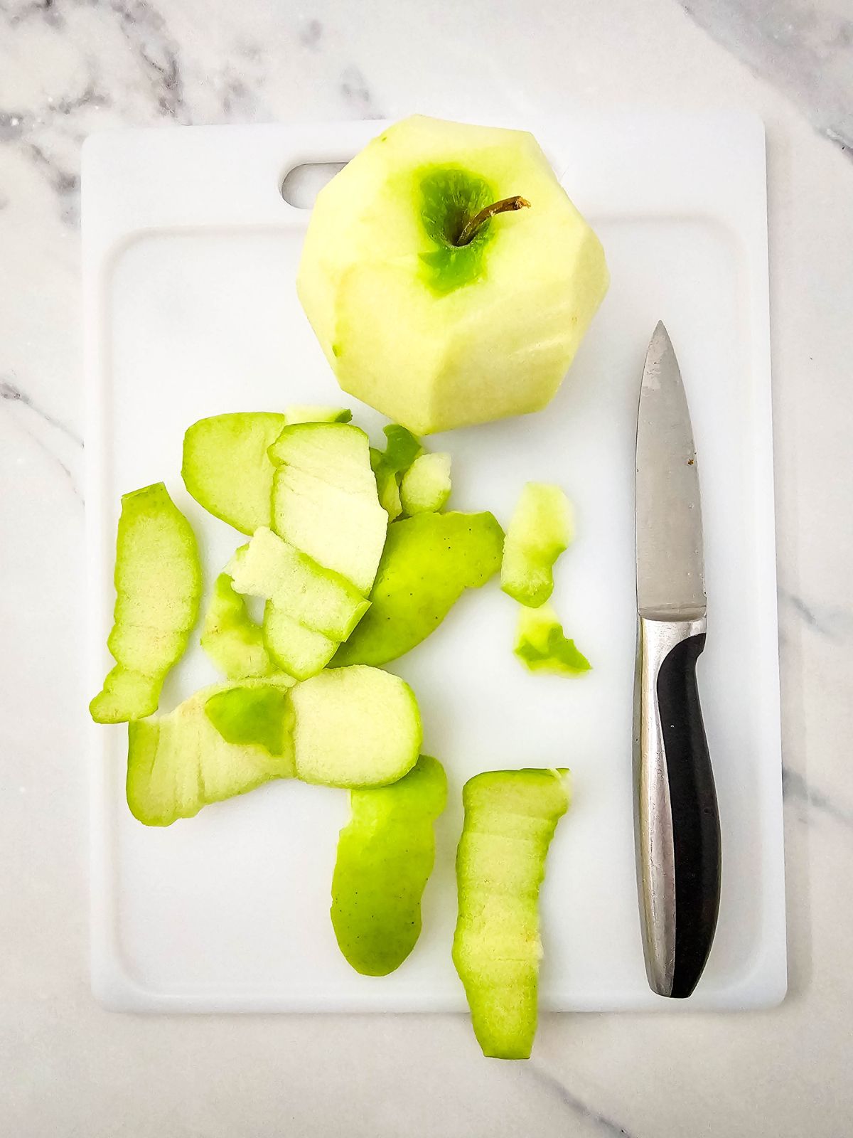 A green apple is peeled on a cutting board next to a knife.