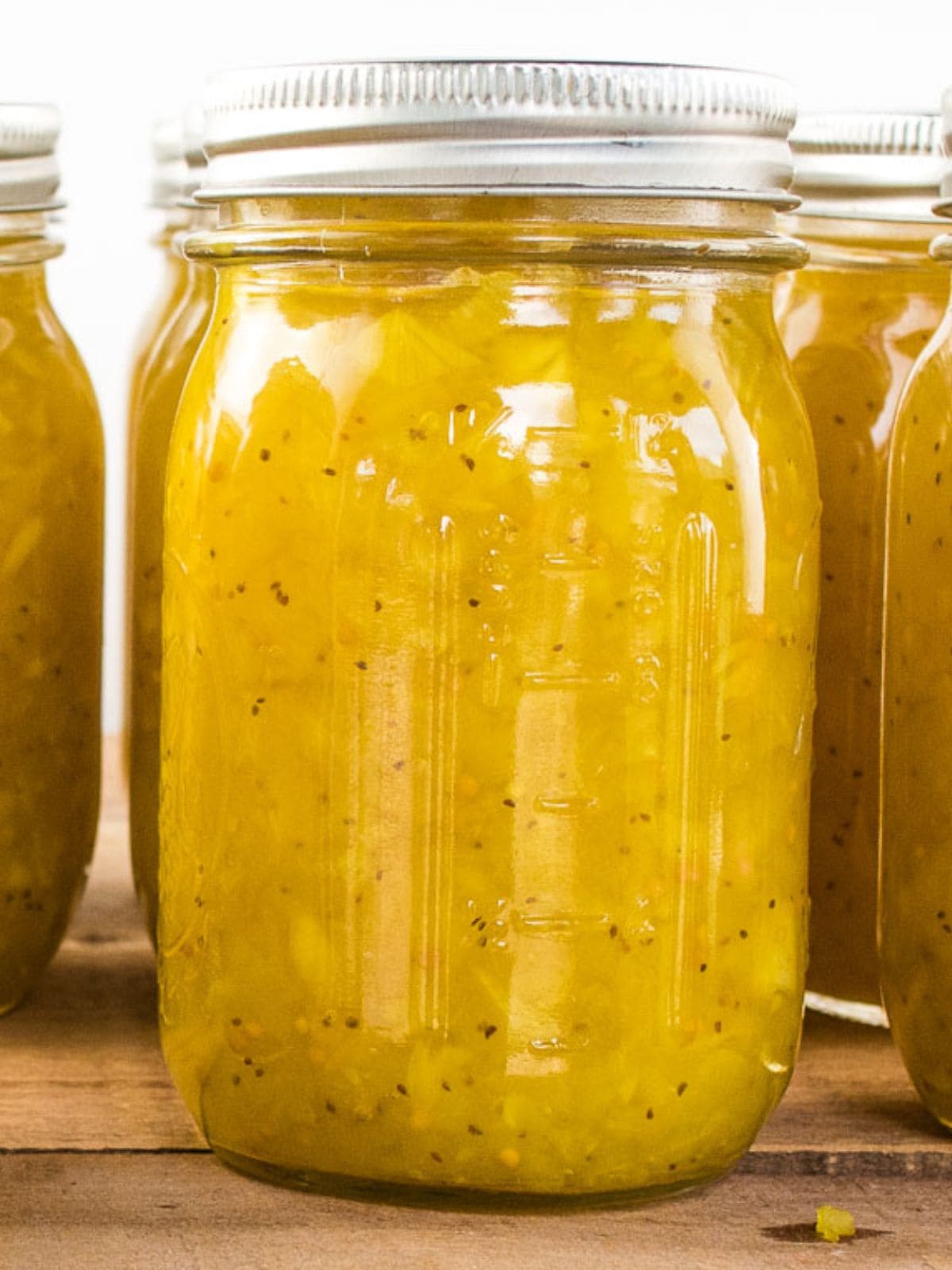 Mason jars of homemade ripe cucumber relish sitting on a wooden table.