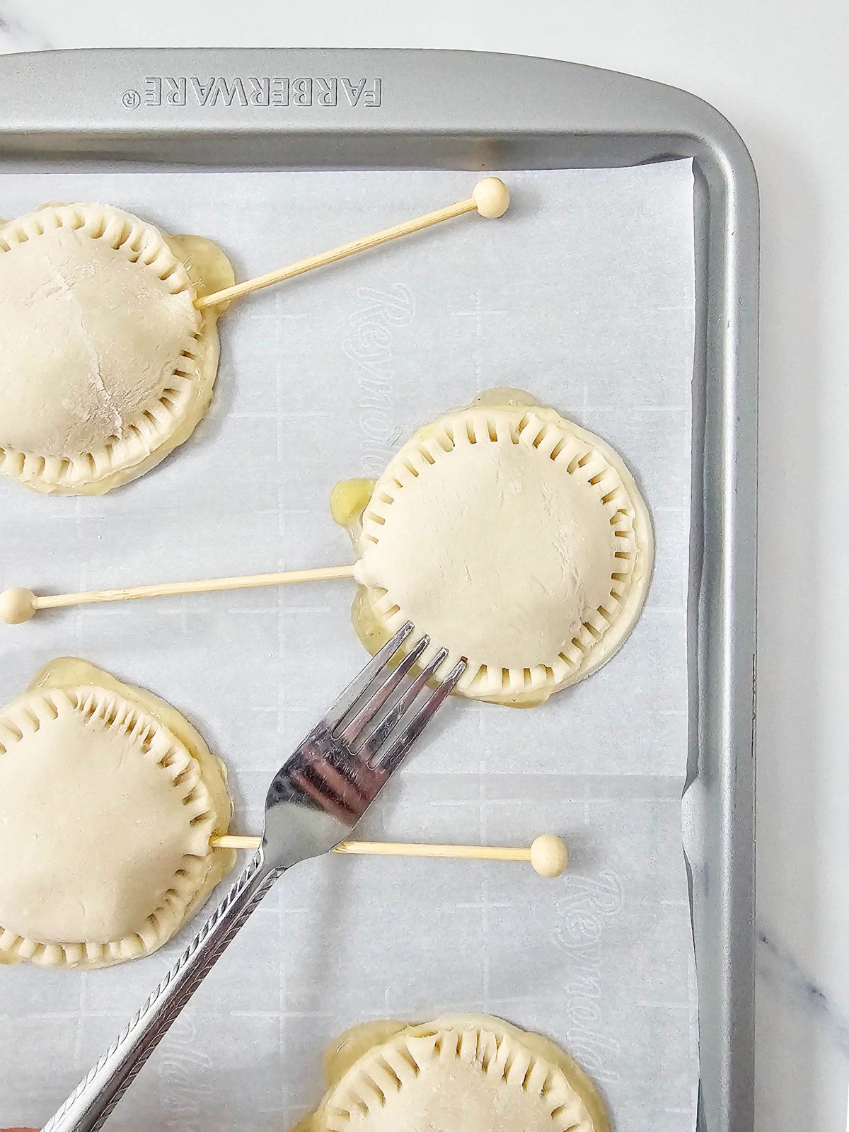 Pressing the edges of the top and bottom pie crust together with a fork to seal them.