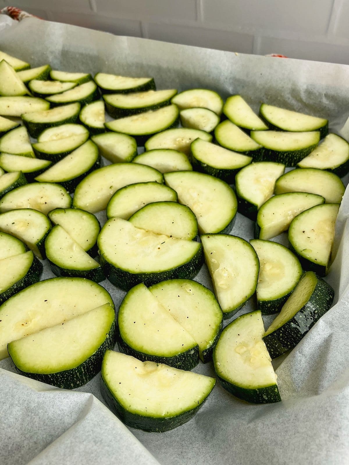 Seasoned zucchini slices spread out on a parchment-lined sheet pan.