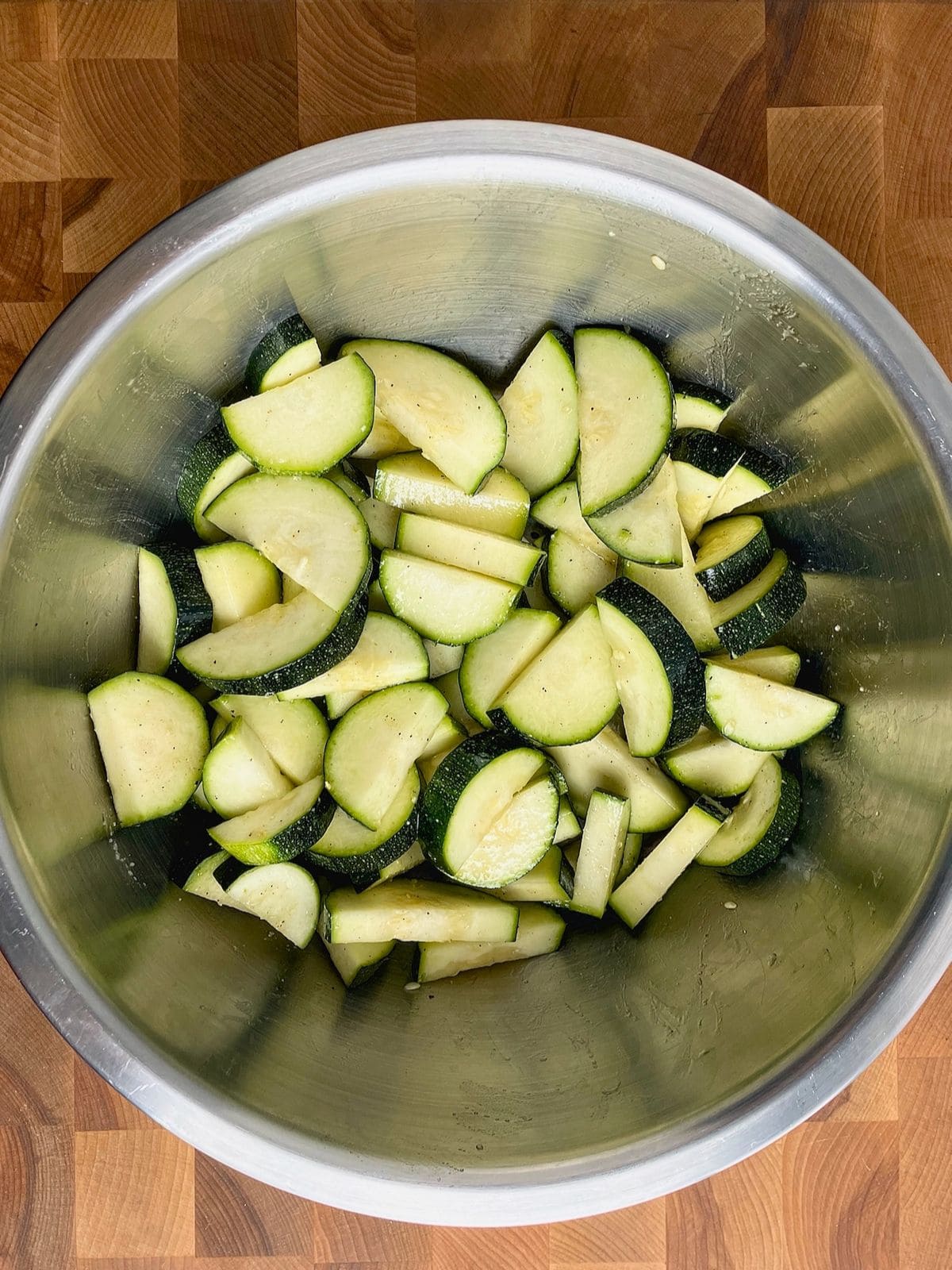 Zucchini slices in a mixing bowl tossed with vegetable oil and seasonings.