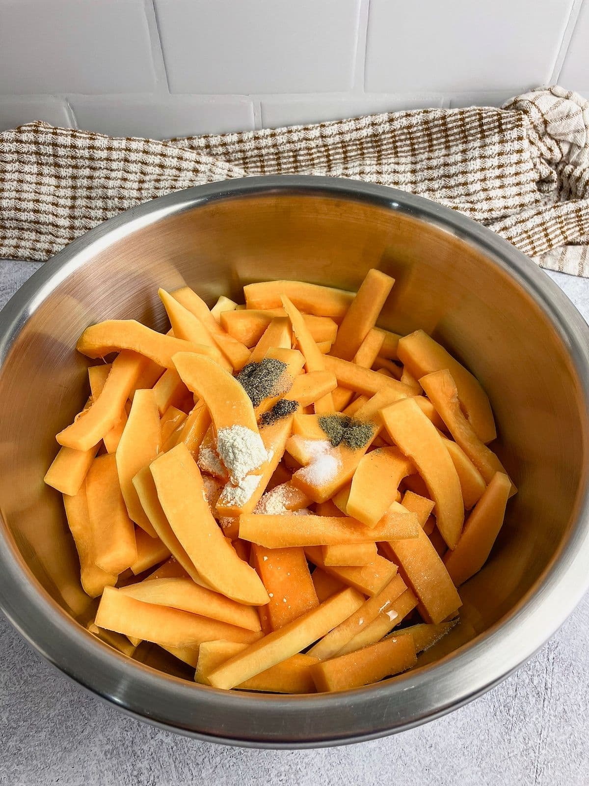 Squash fries in a large mixing bowl with olive oil and seasonings poured on top.