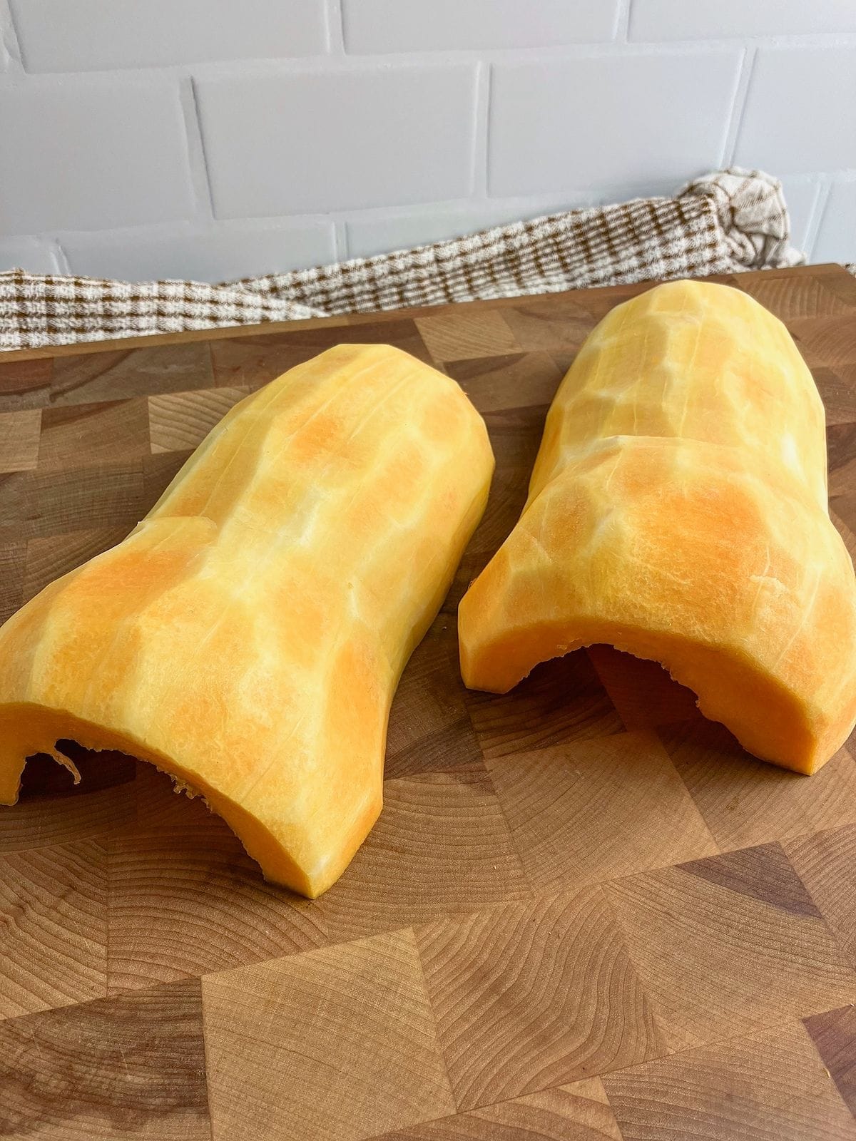 A butternut squash cut in half and seeds removed on a cutting board.