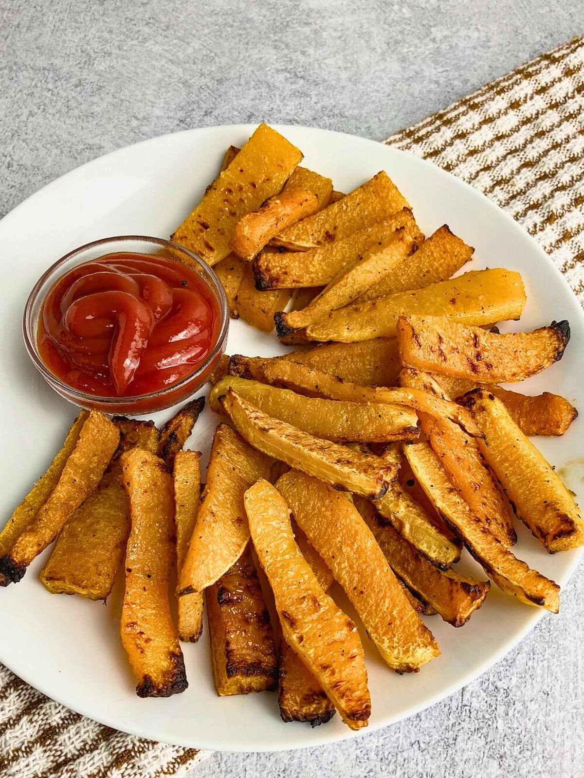 Easy homemade butternut squash fries on a plate with ketchup dip.