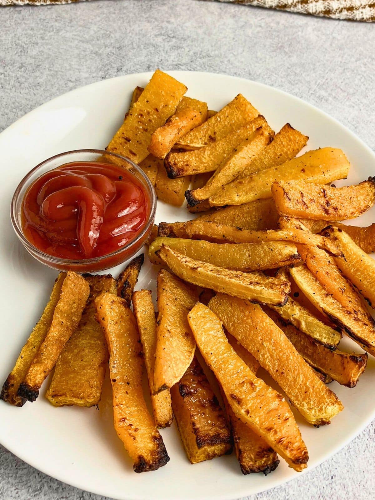 Baked butternut squash fries on a plate with ketchup.