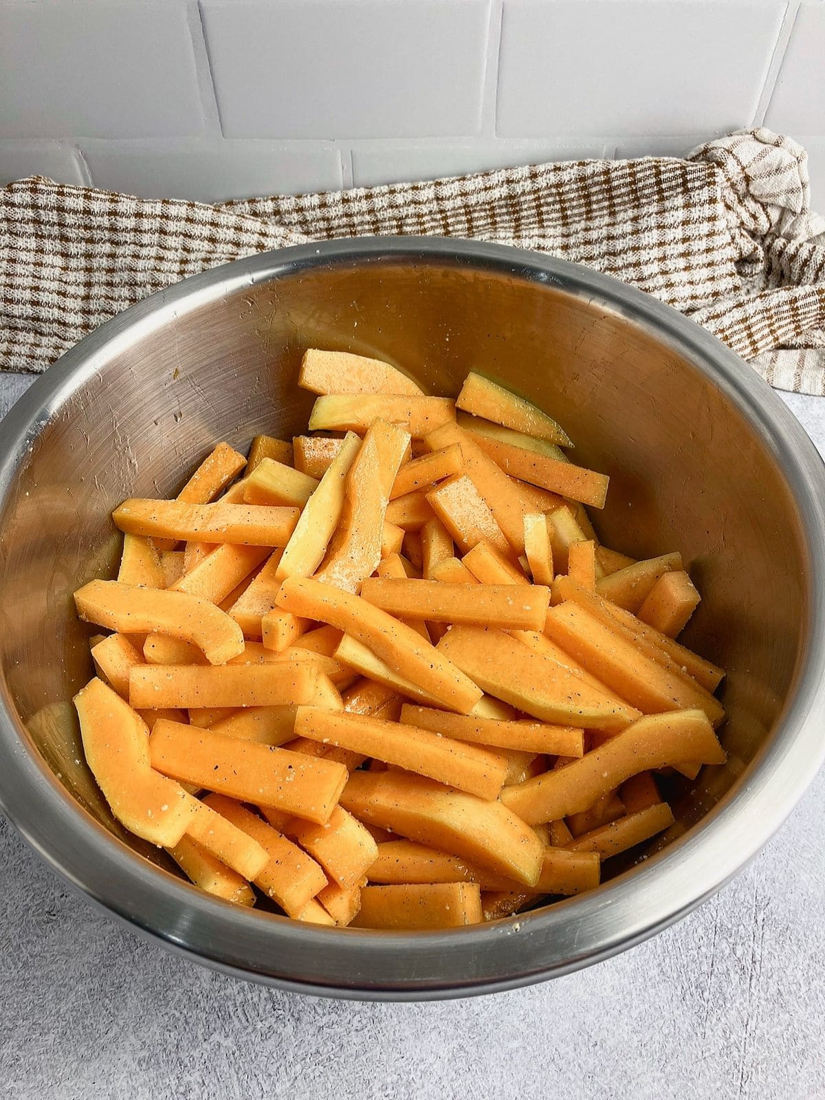 Squash fries in a bowl tossed with oil and spices.