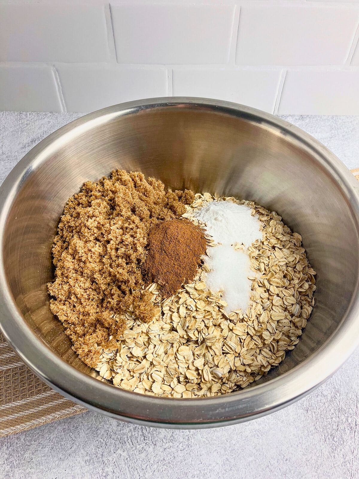 A large mixing bowl with rolled oats, brown sugar, cinnamon, nutmeg, salt, and baking powder.