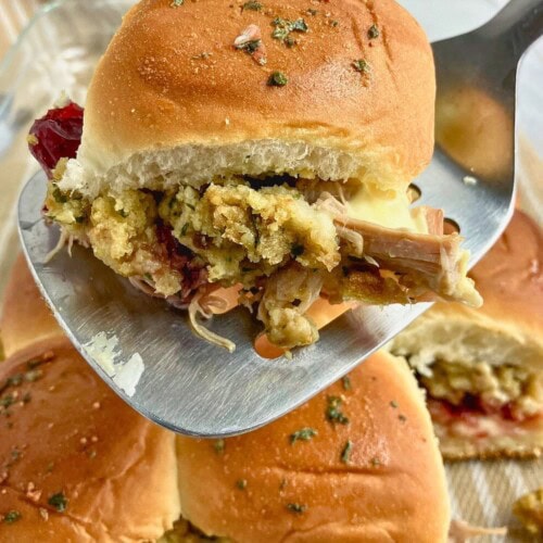 Lifting a leftover turkey slider out of the baking dish with a spatula.