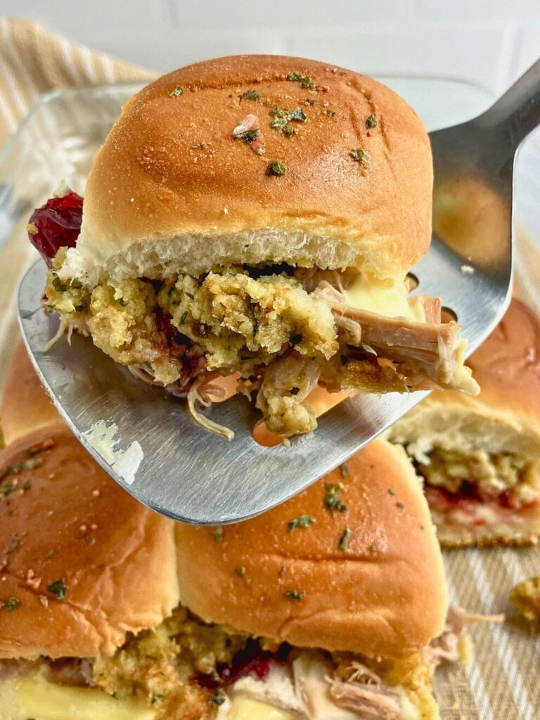 Lifting a leftover turkey slider out of the baking dish with a spatula.