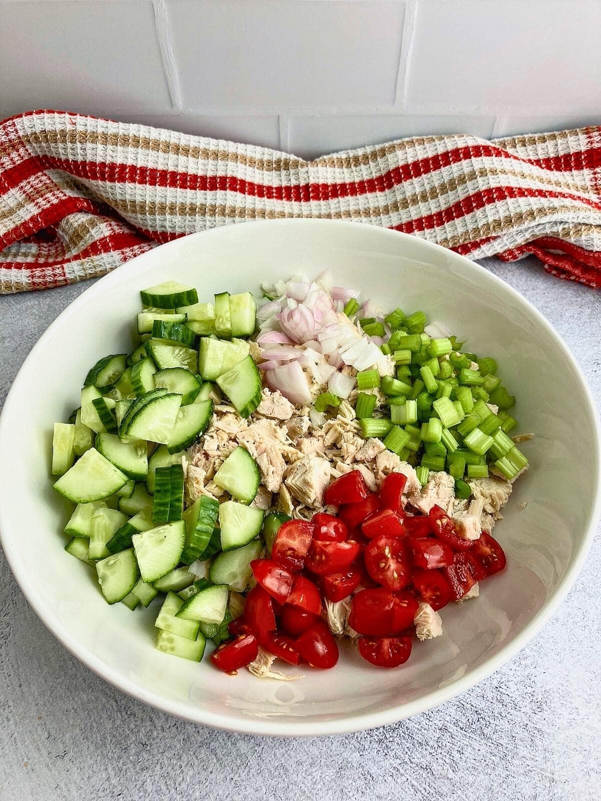 Celery, red onion, cucumber, and tomatoes were added to the chicken in a large bowl.