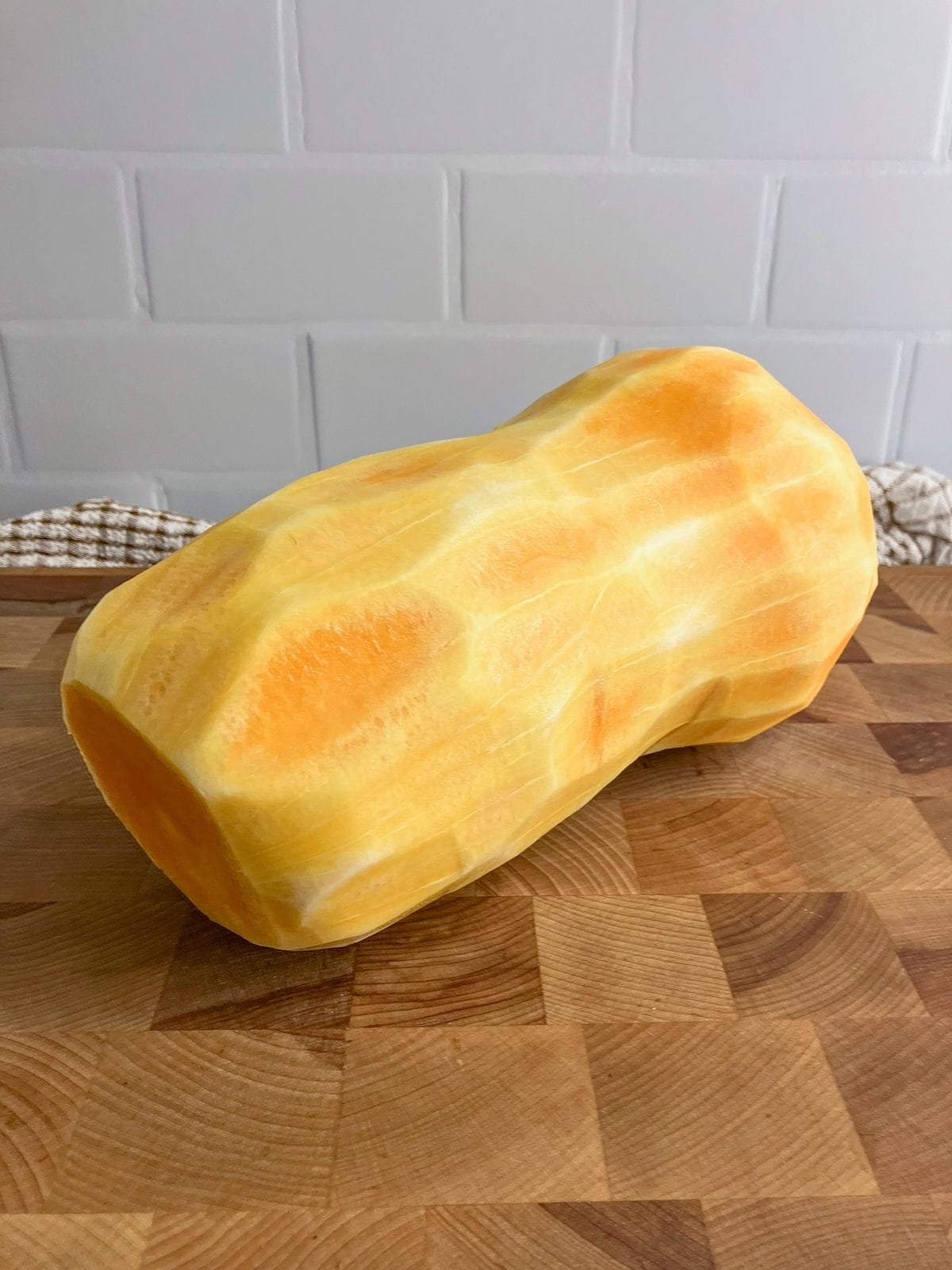 A whole butternut squash, peeled and sitting on a cutting board.