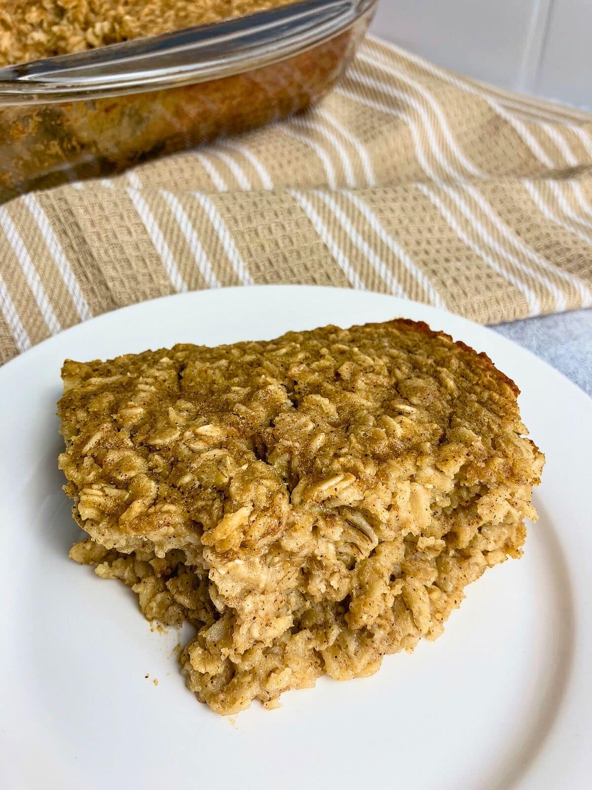A slice of pumpkin baked oatmeal on a white plate next to a baking dish.