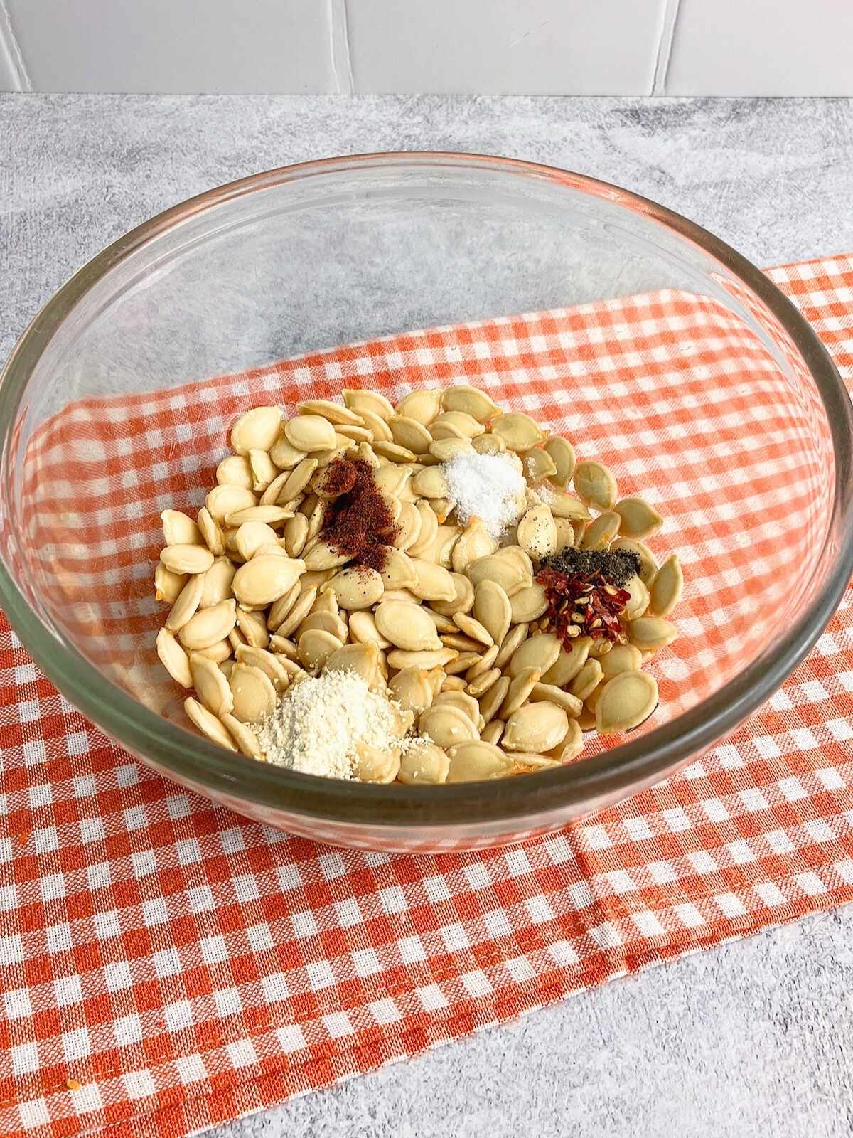 Vegetable oil, salt, and spices were added to the raw pumpkin seeds in a mixing bowl.