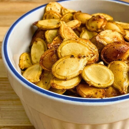 Homemade spicy roasted pumpkin seeds in a small white bowl.
