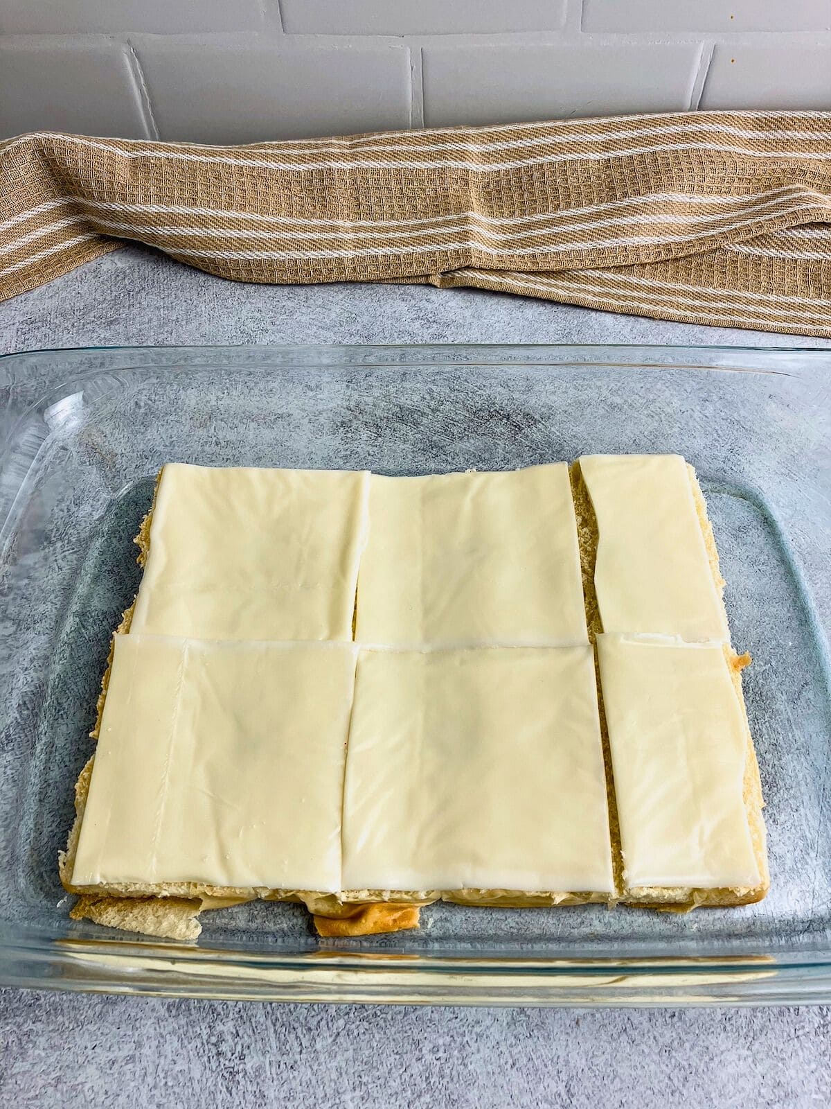 Slices of Swiss cheese are layered over the bottom rolls.