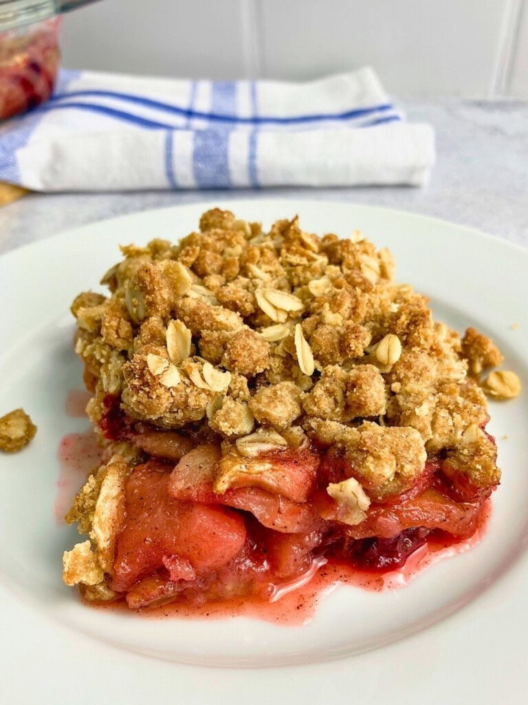 A slice of homemade apple cranberry crisp on a white plate.