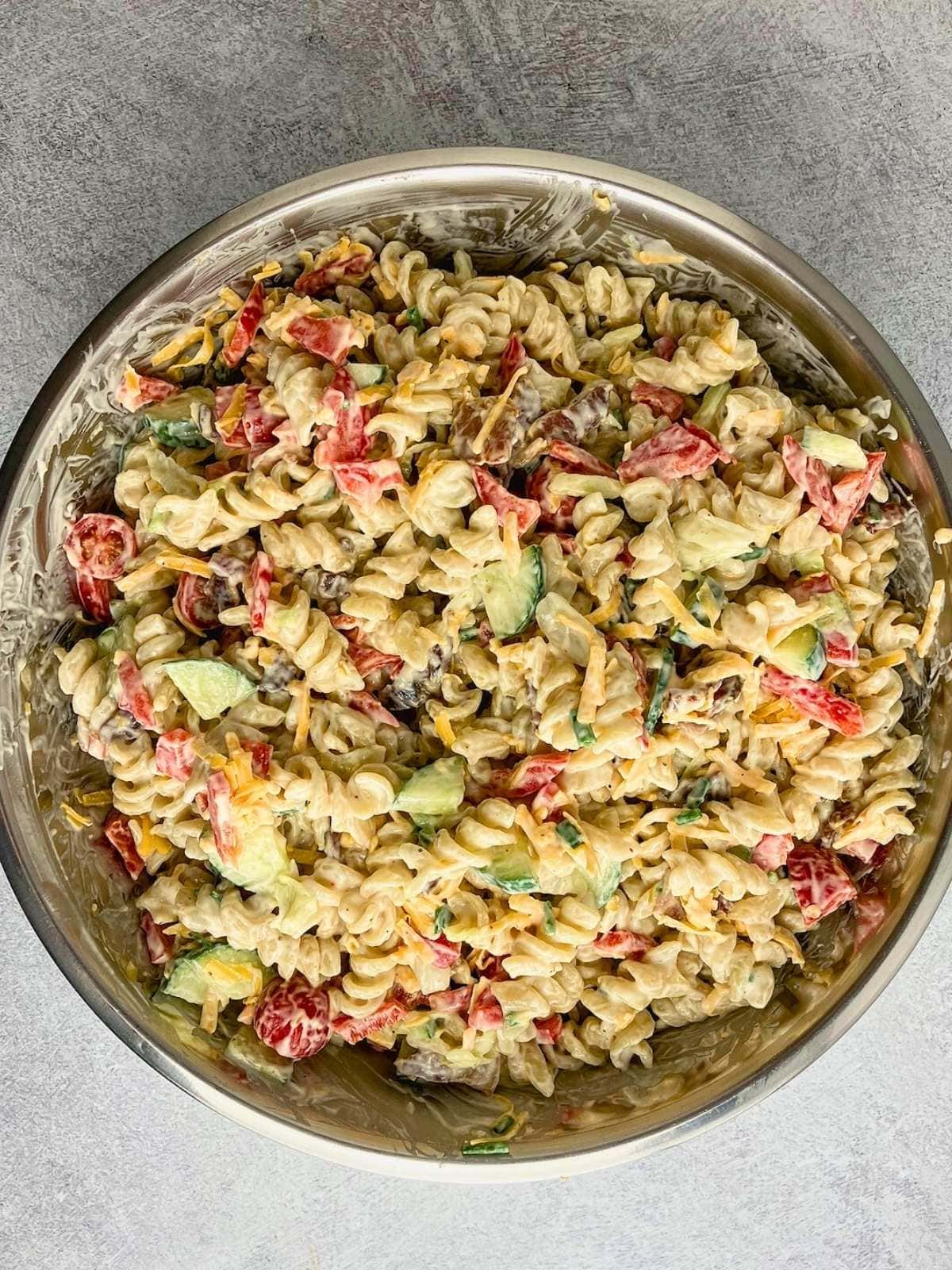 Bacon pasta salad is mixed together in a large bowl.