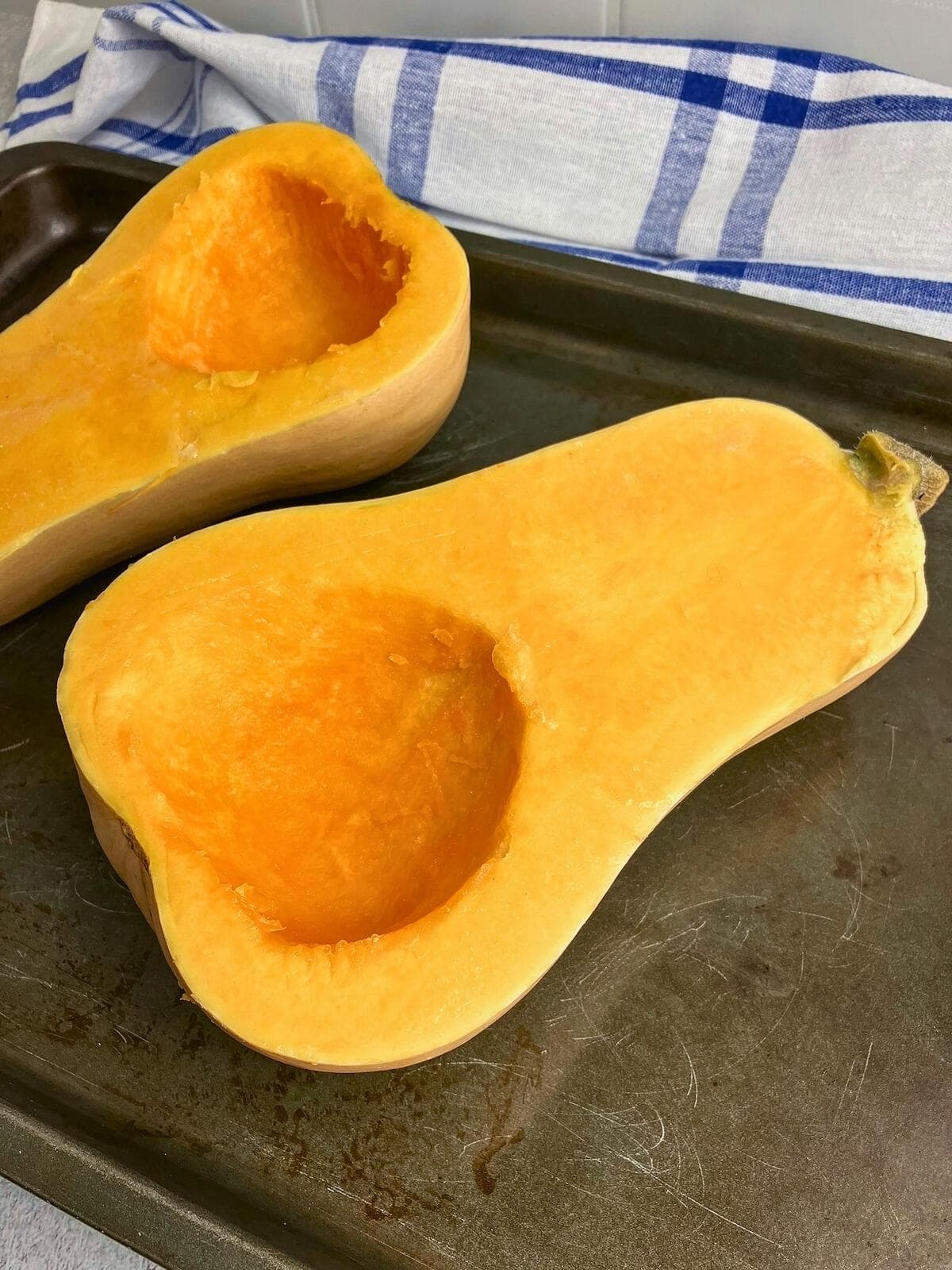 A butternut squash is cut in half, with the seeds removed, and placed on a baking sheet.