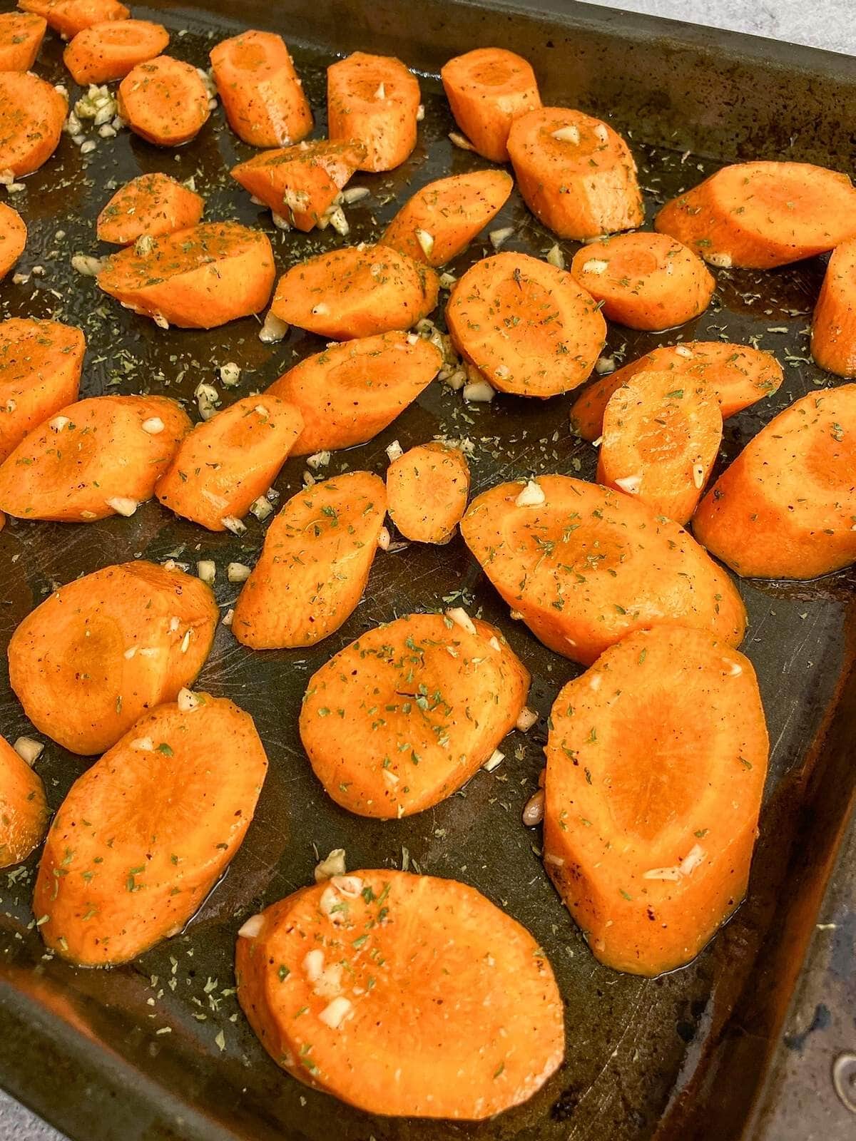 Seasoned sliced carrots are spread on a baking sheet.