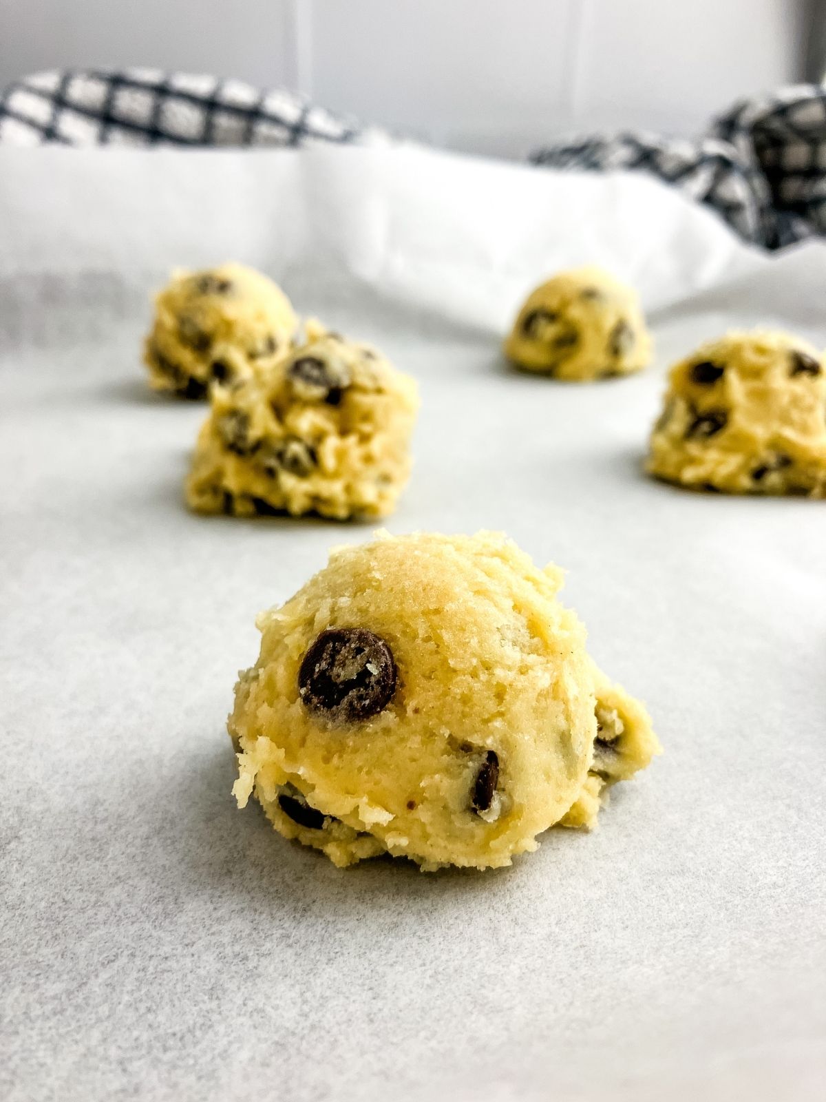 Chocolate chip cookie dough balls on a parchment-lined baking sheet.