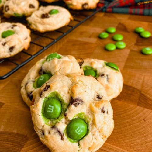 Homemade Christmas chocolate chip cookies on a wooden table next to a cooking rack of cookies.