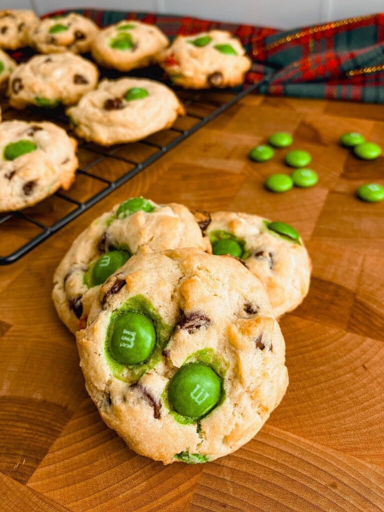 Homemade Christmas chocolate chip cookies on a wooden table next to a cooking rack of cookies.