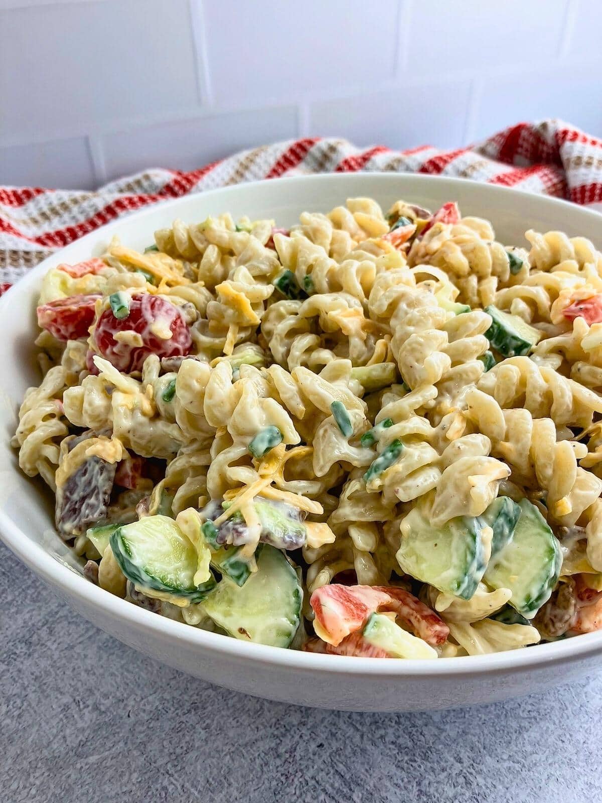 Creamy bacon pasta salad with cheese and veggies in a large bowl.