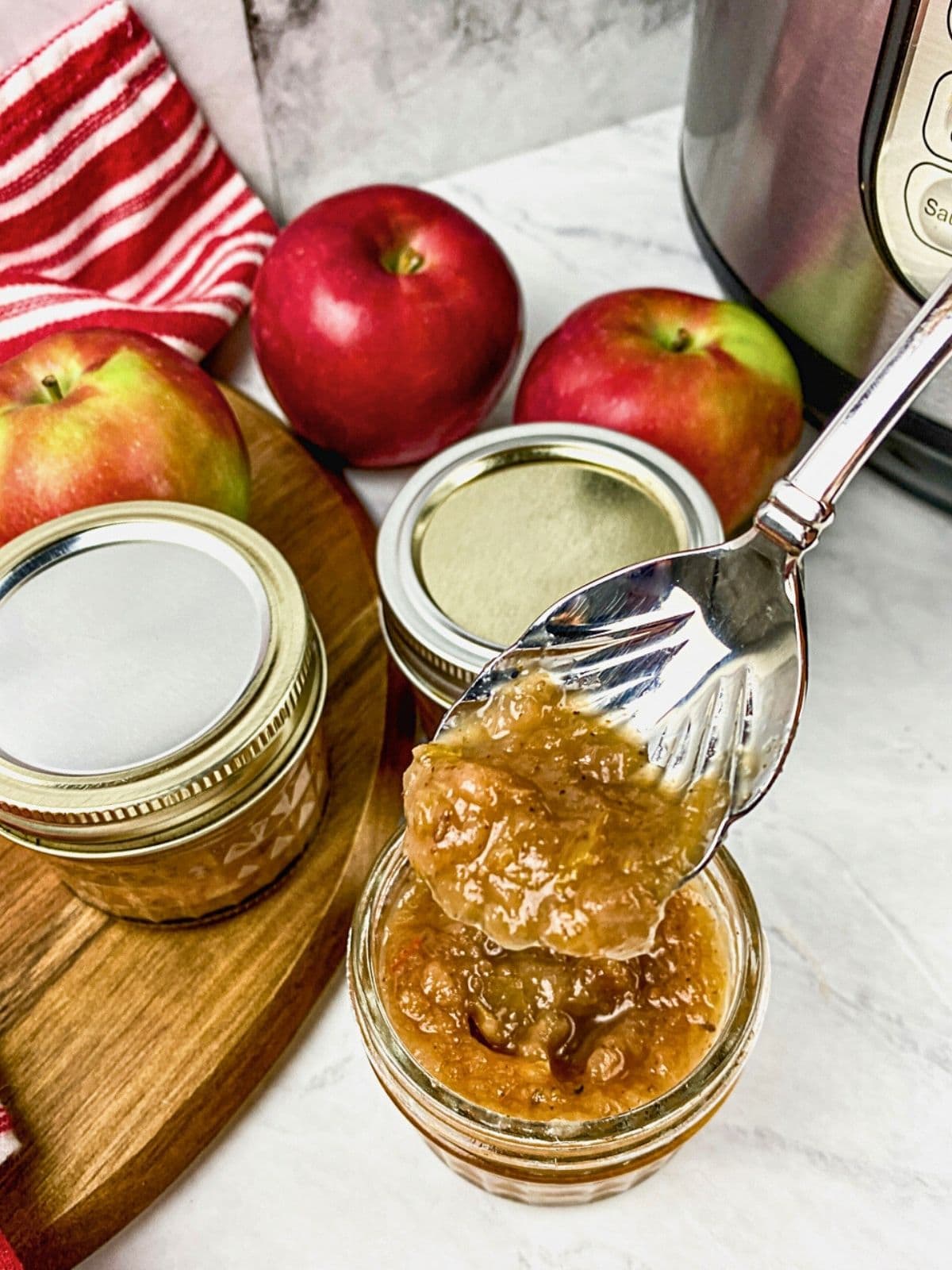 Apple chutney cooked in the Instant Pot and put into mason jars. A spoon is lifting up a serving of apple chutney over the jar.