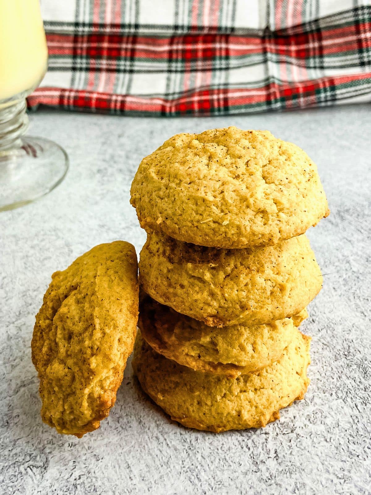 Homemade soft and chewy eggnog cookies stacked on the counter next to a glass of eggnog.