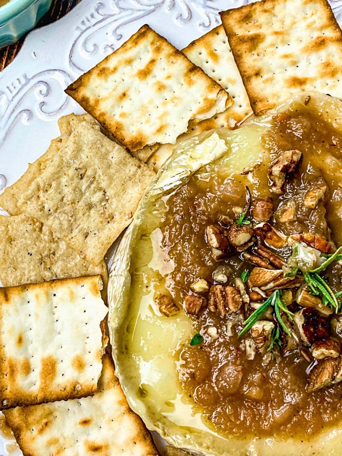 Baked brie with spiced apple and pecan topping on a platter with crackers.