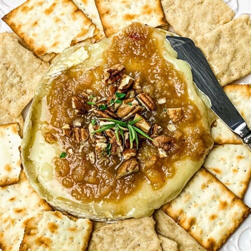 Instant Pot baked brie with apple and pecan topping on a platter with crackers.